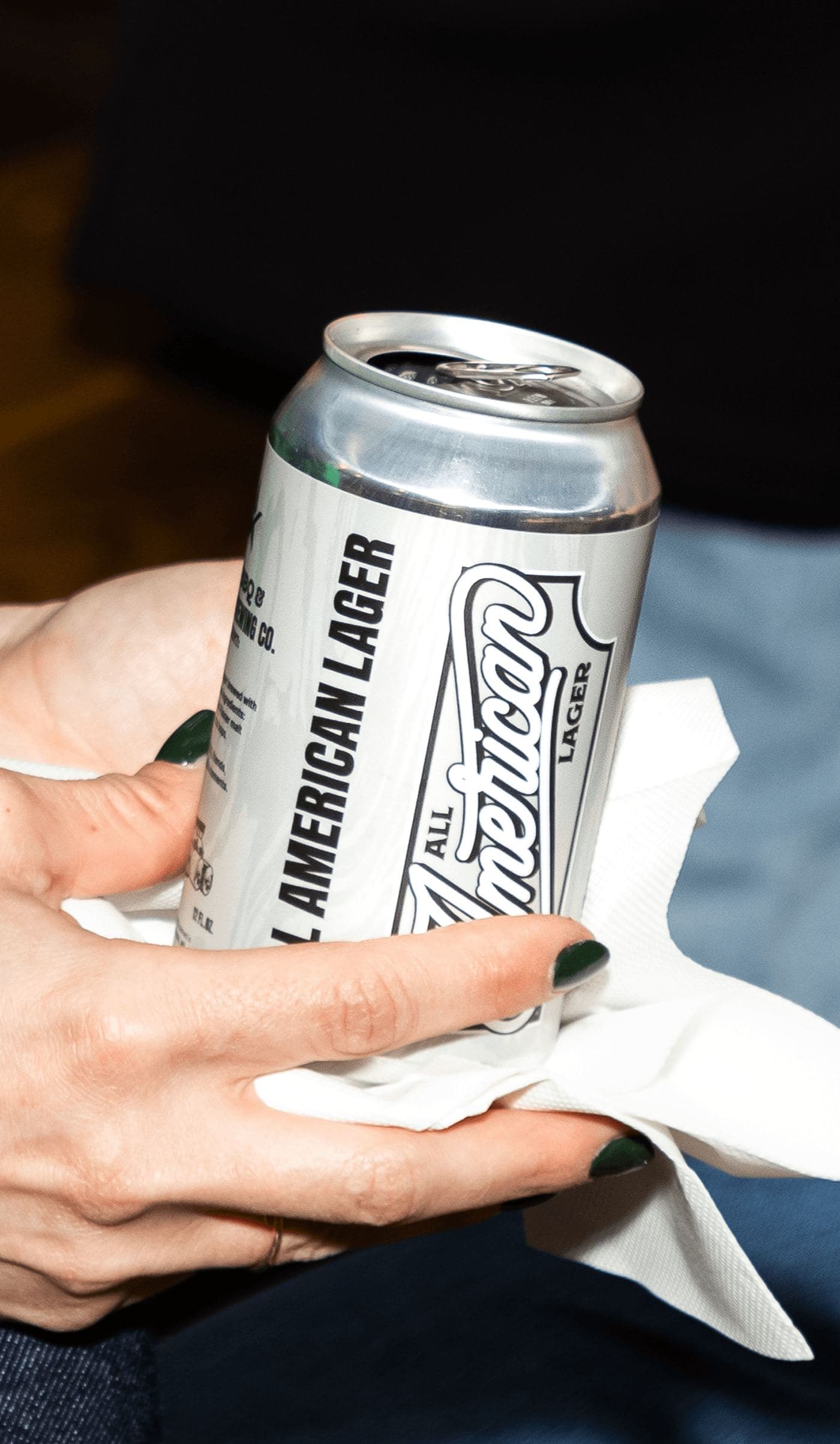 A hand holding a can of All American Lager with a napkin