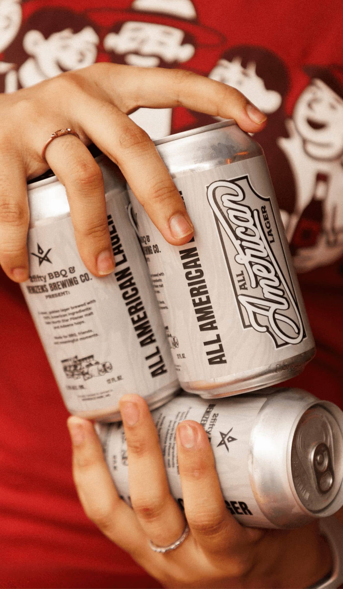 Hands passing cans of All American Lager against a red 2fifty backdrop