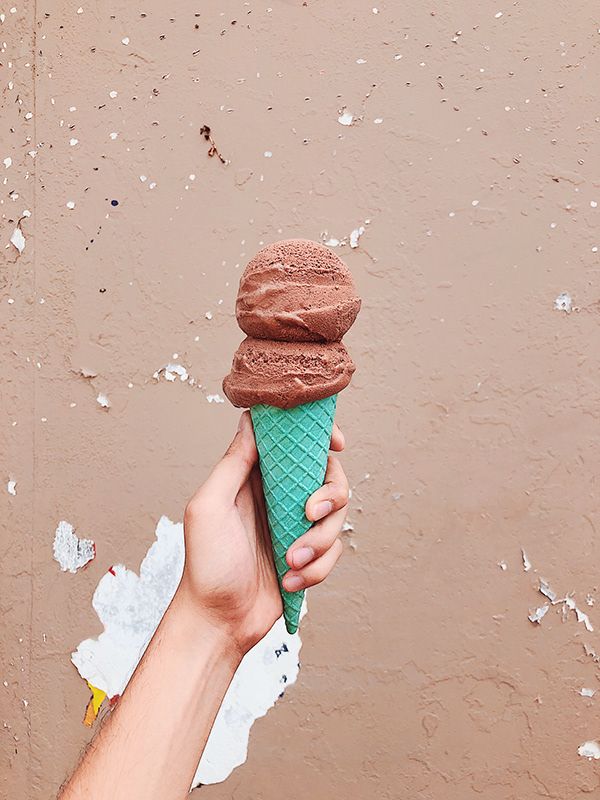 A chocolate ice-cream cone in a teal cone against a peeling wall