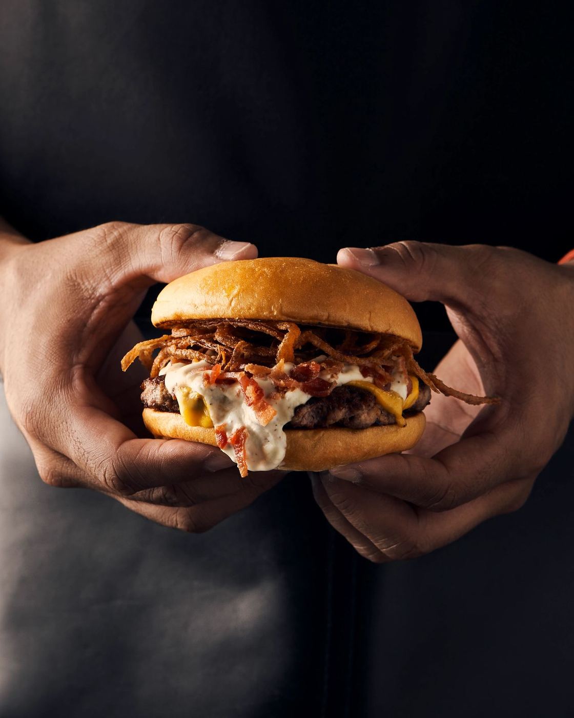 La Diosa burger held in both hands against a dark apron