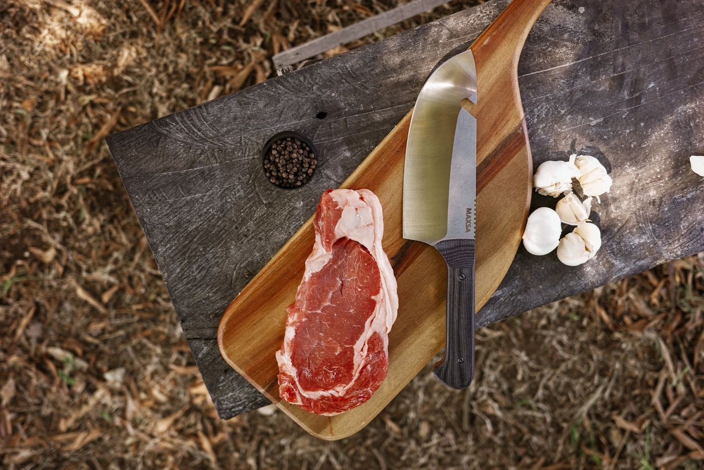 MAXSA blade on a wooden board with steak, garlic and peppercorns