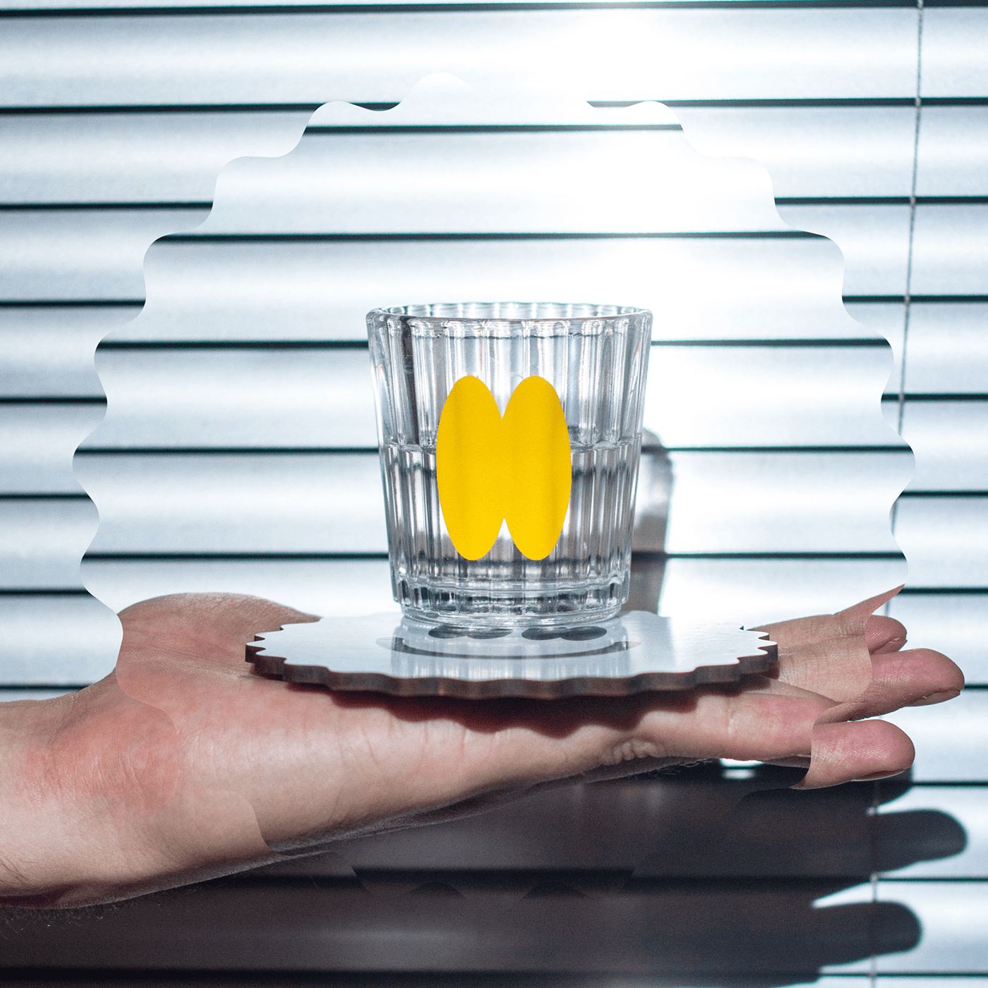 A glass on a scalloped coaster held on an open palm, striped light behind
