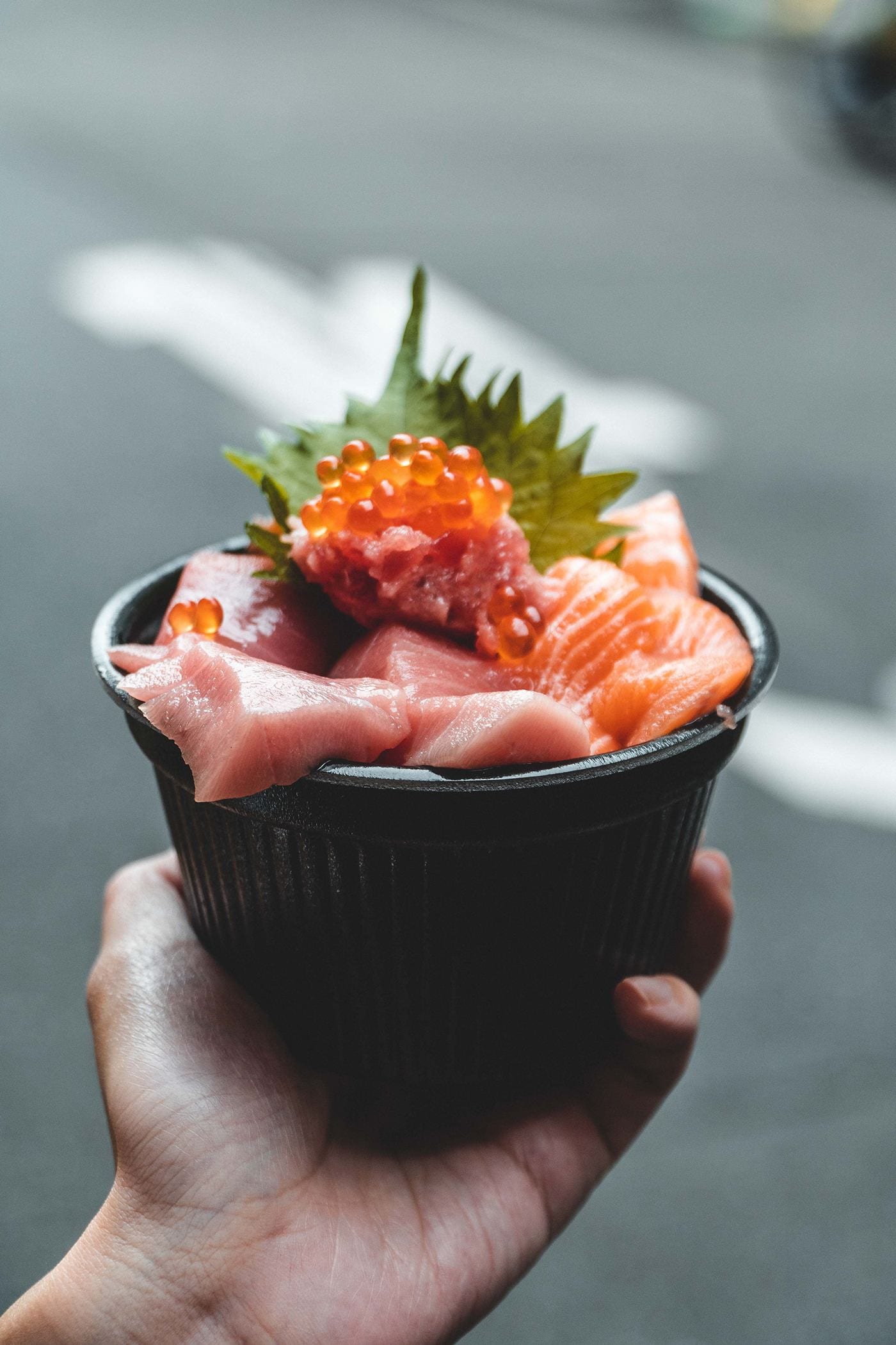 A hand holding a bowl of raw fish and salmon roe